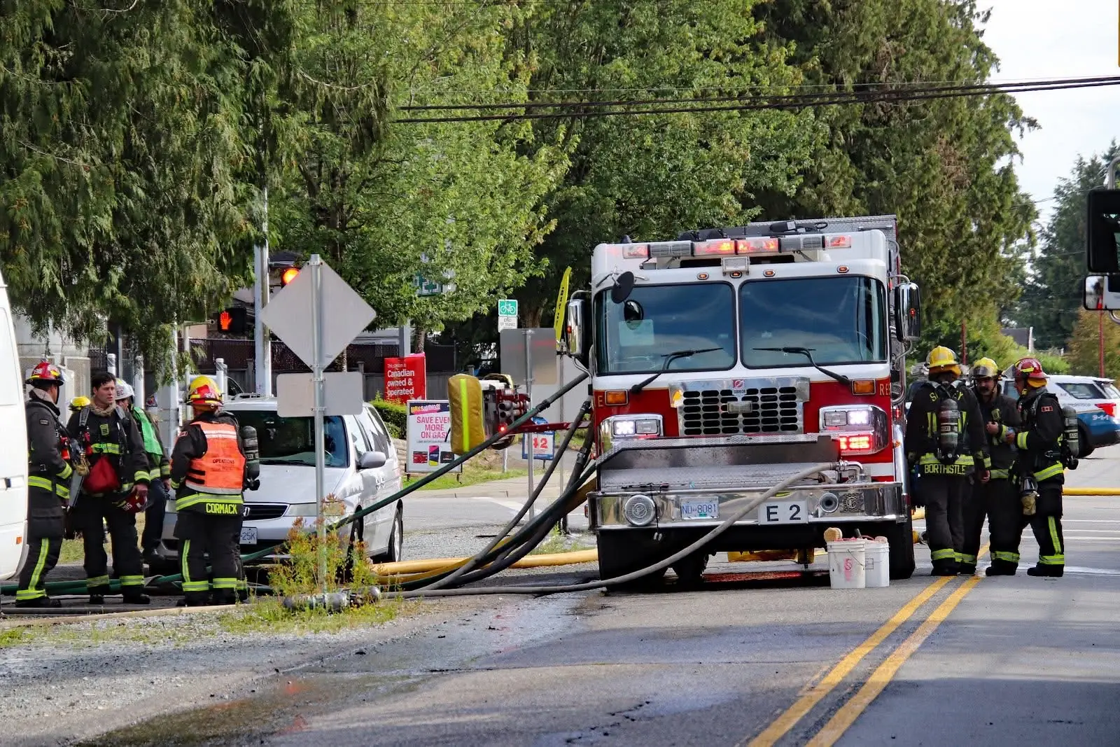 Surrey fire fighters standing beside Engine 2 on a residential street, with hose lines run out across the road.